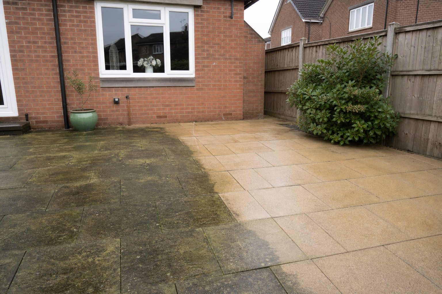 Garden patio half cleaned by jet washing with a sharp line between green-stained and clean slabs